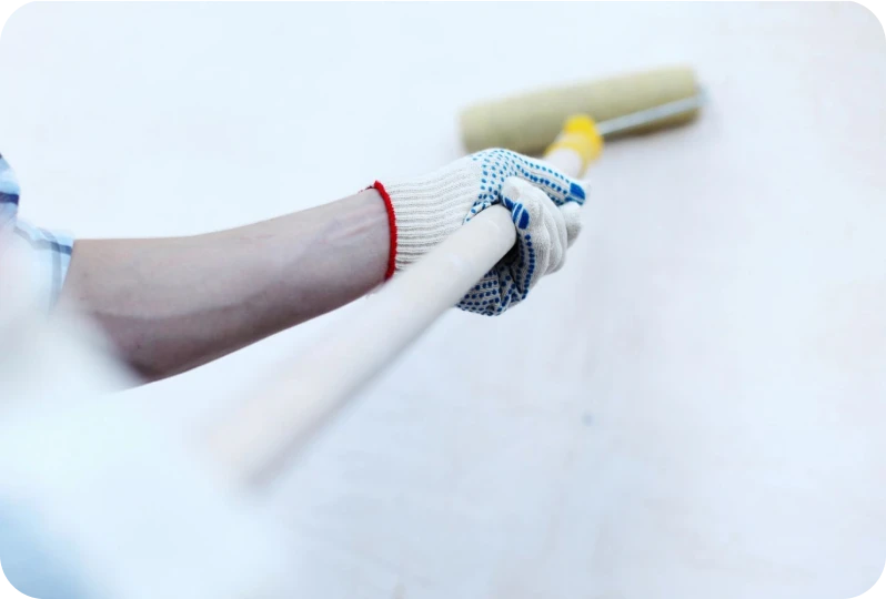 Gloved hand using paint roller on wall