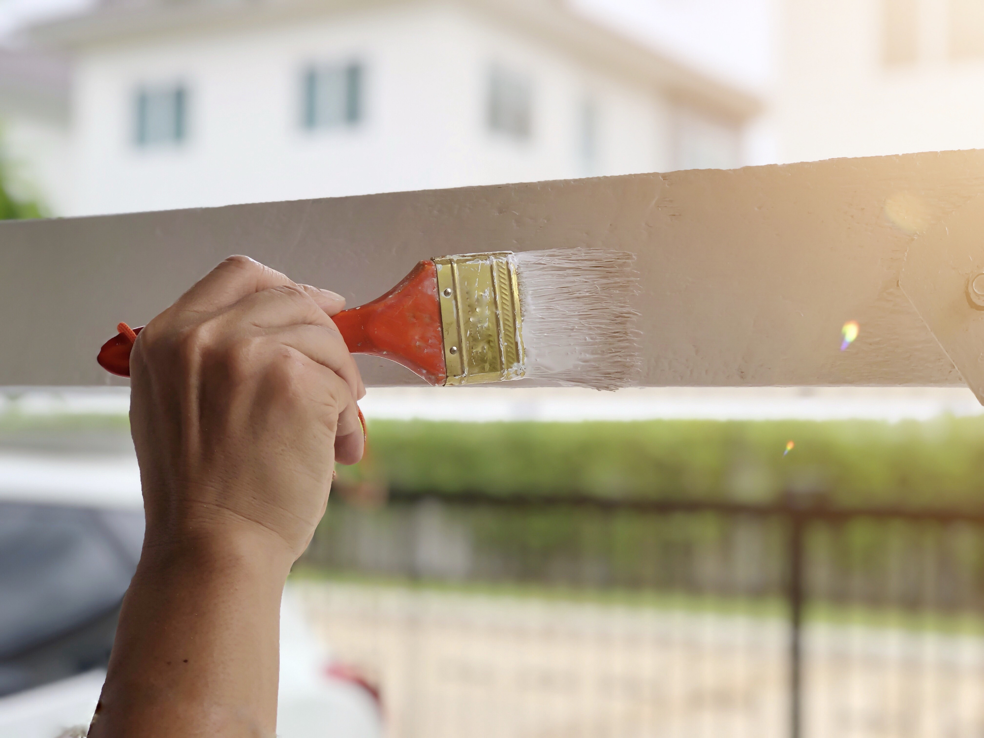 Painter’s hand painting with brush on wooden table. Hand Man holding paint brushes with blurred background of car and house. Home decorations and interior design concept